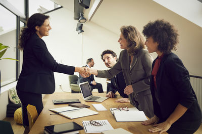 Smiling businesswoman greeting senior female lawyer at conference table during meeting in office