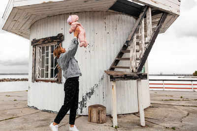 Side view of woman holding son mid air by built structure