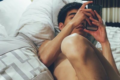 Shirtless man using mobile phone while lying on bed