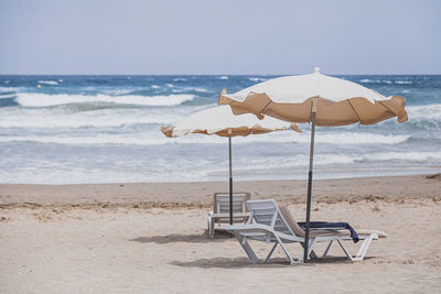 Deck chairs on beach against sky