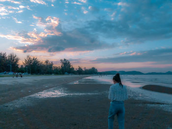 Rear view of woman standing on land against sky during sunset