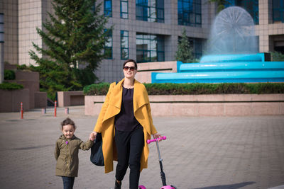 Mother and daughter walking on footpath in city