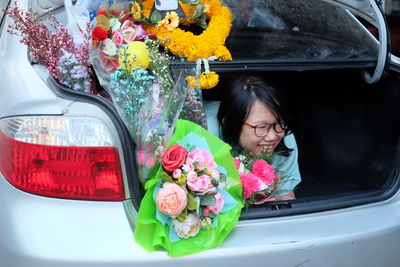 Happy young woman with bouquets sitting in car trunk