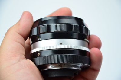 Cropped hand holding camera lens against white background