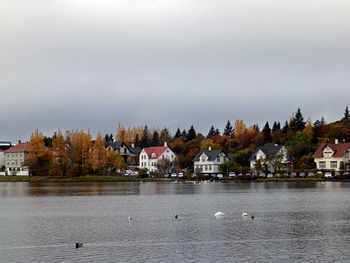 View of lake by houses against sky during autumn