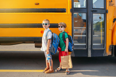 Full length portrait of boys while standing on road by bus