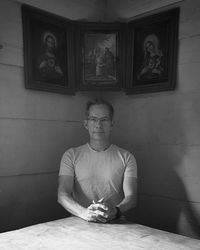 Portrait of man sitting at table against wall