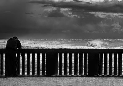 Rear view of man standing by railing against sea