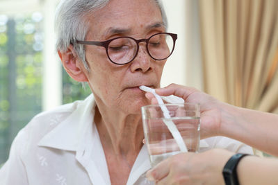 Cropped hand of nurse feeding water to senior woman