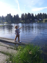 Boy standing by lake against sky