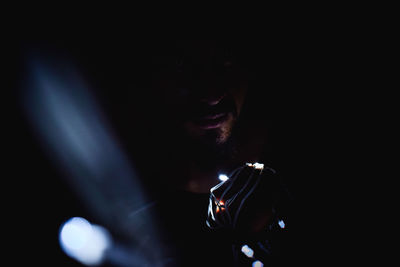 Close-up of young man holding illuminated string light in darkroom