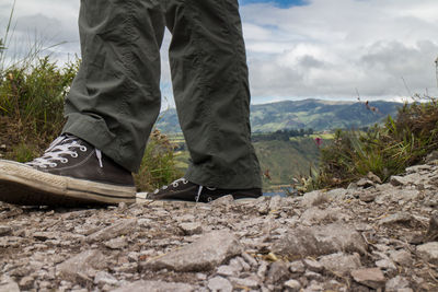 Low section of man standing on mountain against sky