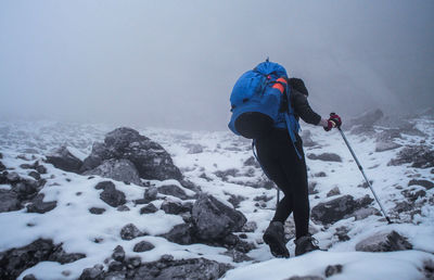 Low angle view of mid adult woman with backpack hiking on snow covered mountain