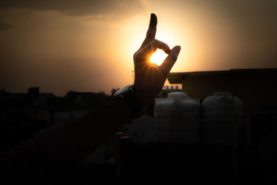 Silhouette hand against orange sky during sunset