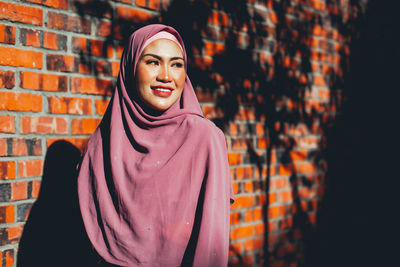 Portrait of smiling young woman standing against brick wall