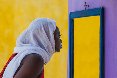 African ghana woman standing in front of a mirror with a white shawl covering her hair
