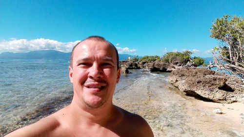 Shirtless man on shore at beach against sky during sunny day