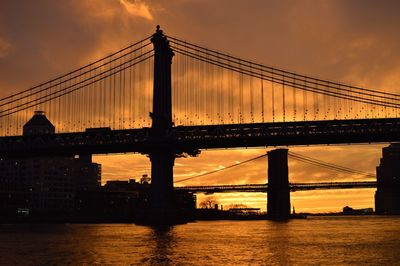 Low angle view of silhouette brooklyn bridge over river against orange sky