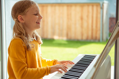 Side view of smiling girl playing piano at home