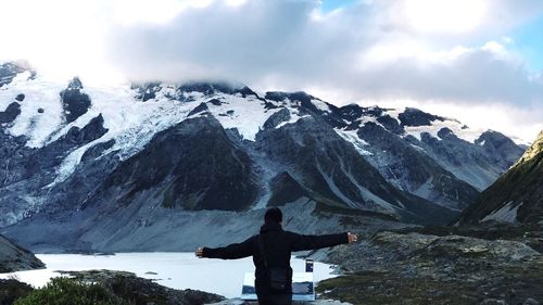 Rear view of man with arms outstretched against snowcapped mountain 