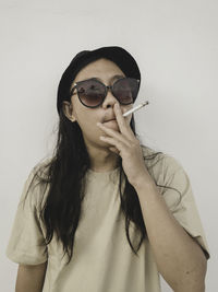 Portrait of young woman wearing sunglasses against white background