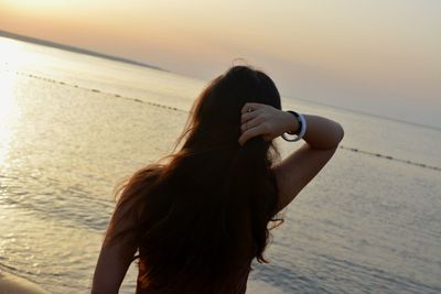 Rear view of woman standing at beach during sunset