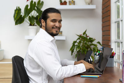 Portrait of young man using mobile phone while sitting on table