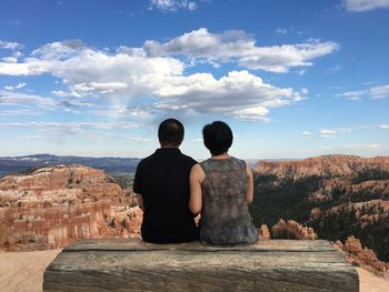 Rear view of couple sitting on rock against sky