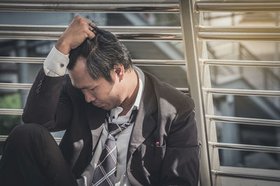 Close-up of depressed businessman sitting against railing