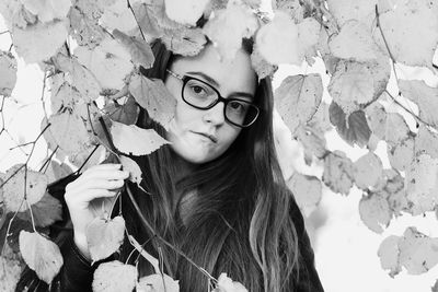 Portrait of young woman standing against leaves
