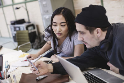 Young woman and man using smart phone at desk in office