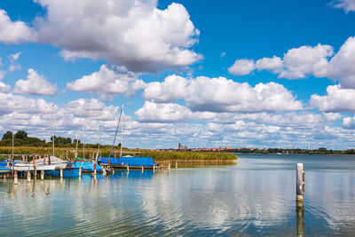 Sailboats moored in lake against cloudy sky