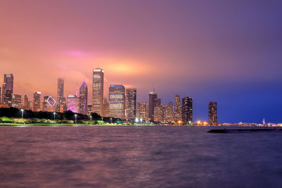 Illuminated buildings by sea against sky