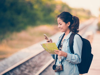 Young woman using phone while standing at railroad station