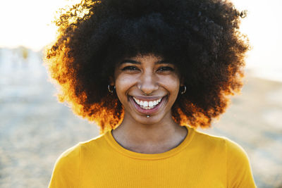 Smiling woman with afro hairstyle at beach during sunset