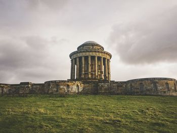 Old ruins on field against cloudy sky