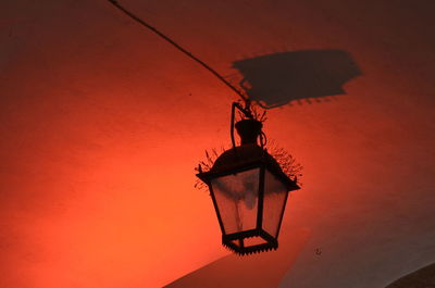 Low angle view of silhouette bird perching on orange wall