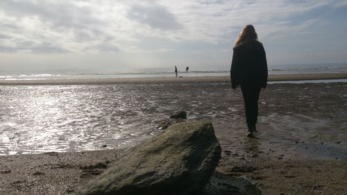 Rear view of woman standing on beach against sky