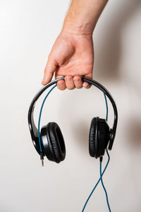 Cropped hand of person holding headphones against wall