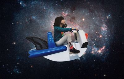 Digital composite image of girl riding model airplane against galaxy