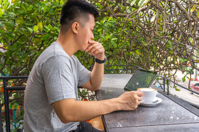Man holding coffee while sitting on plant