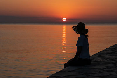 Rear view of silhouette woman standing by sea against sky during sunset