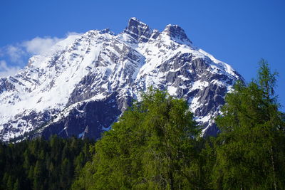 Low angle view of snowcapped mountains against blue sky