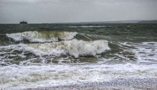 Waves splashing on shore against sky