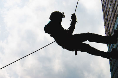 Low angle view of silhouette man holding rope against sky