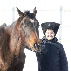 Portrait of boy smiling while standing with horse against wall