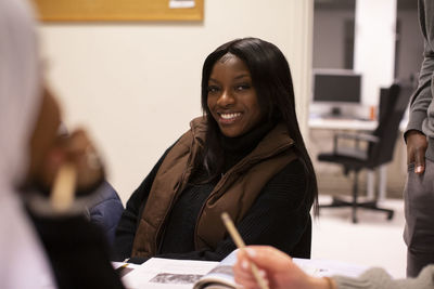 Smiling student with brown jacket sitting in classroom