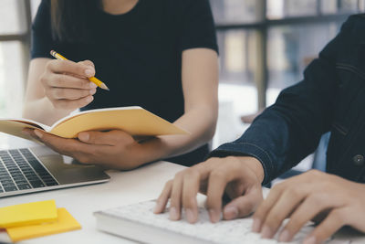 Cropped image of students using laptop while studying on table