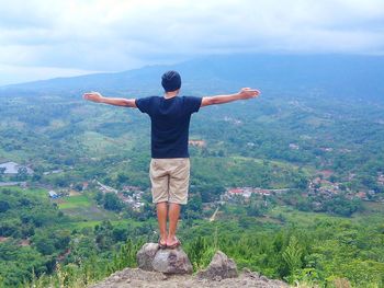 Rear view of man with arms outstretched against sky