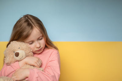 Cute girl embracing teddy bear against wall